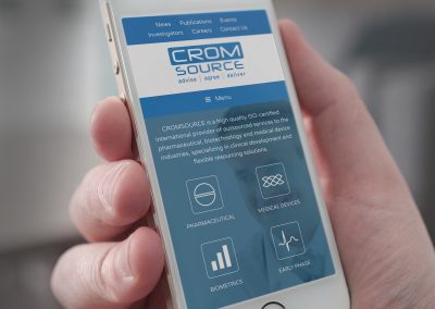 A hand holding a white mobile phone showing a web page called Cromsource